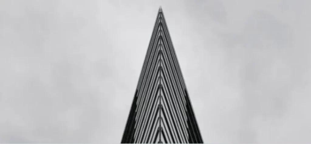 Top view of a modern, triangular glass skyscraper against a gray sky.