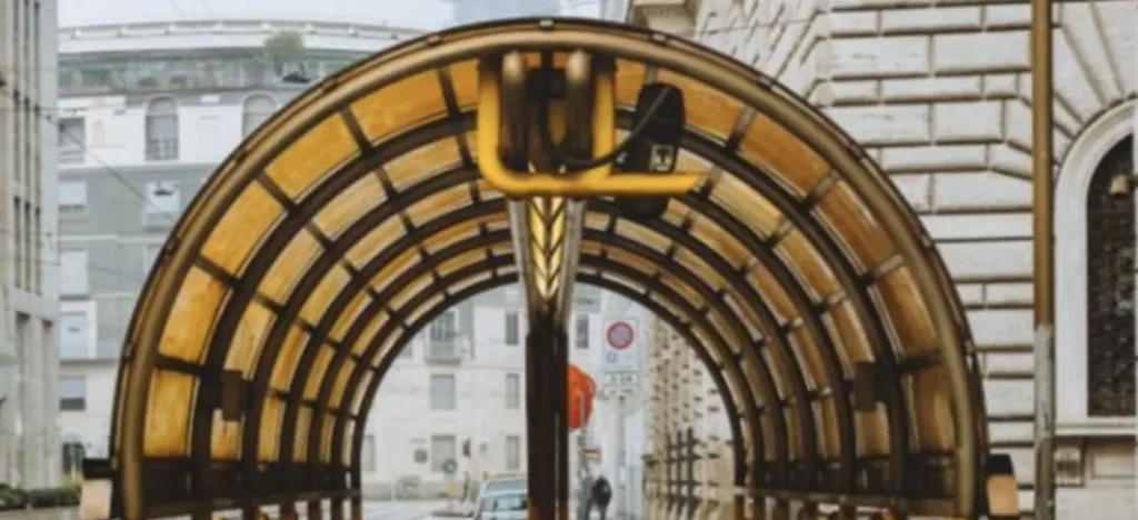 Yellow and black arched bus stop shelter on a city street with buildings in the background.