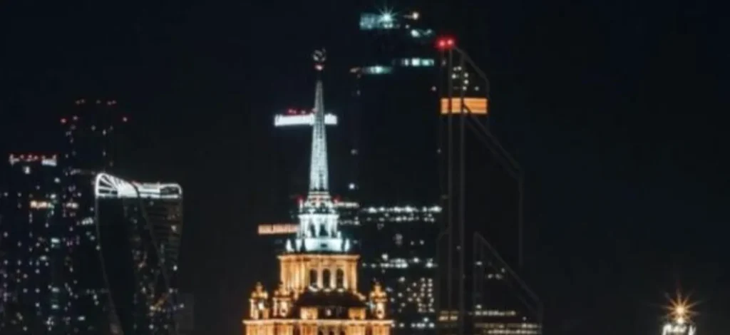 Nighttime cityscape featuring illuminated historic and modern skyscrapers against a dark sky.