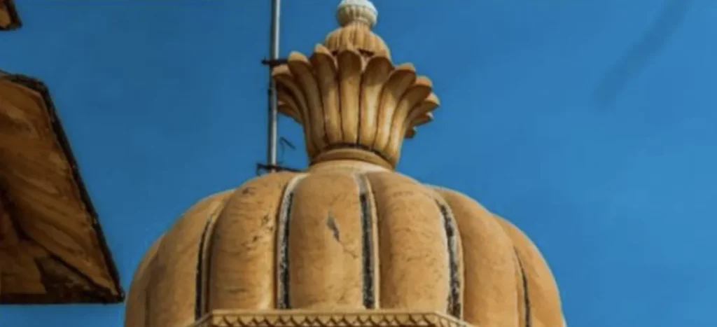 Close-up of a beige stone dome with carved floral patterns against a clear blue sky.