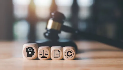 Wooden blocks with legal icons in front of a judge's gavel on a table.