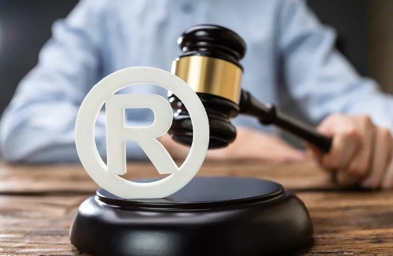 Close-up of a judge's gavel striking a sound block with a registered trademark symbol in foreground.