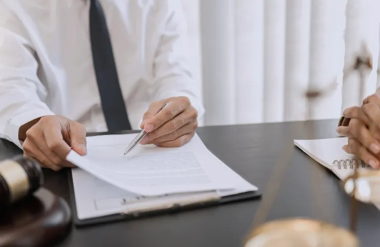 Two individuals at a desk reviewing a document, with a gavel and scales of justice nearby.